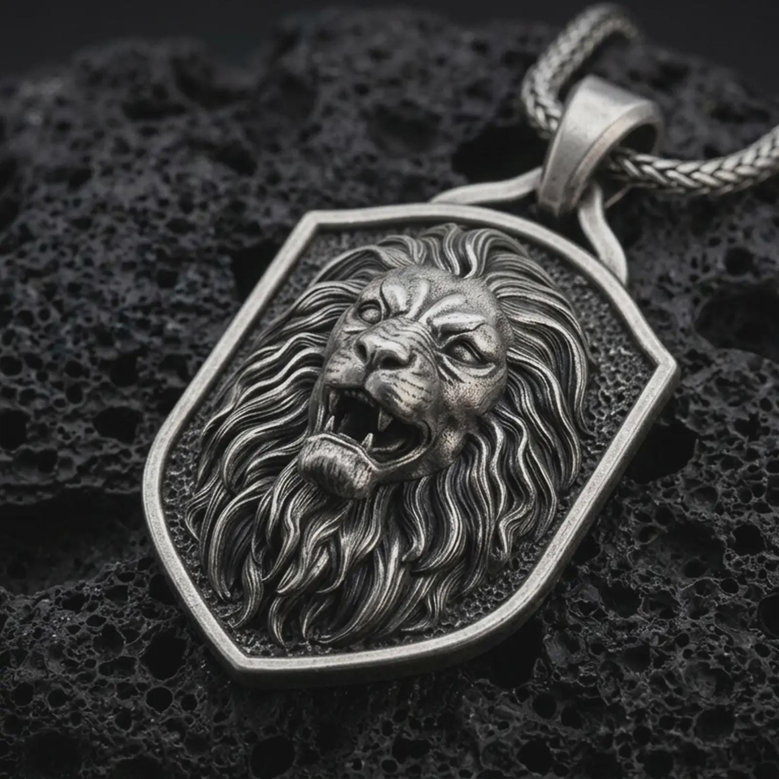 Sterling silver roaring lion shield pendant necklace with an oxidized finish resting on textured volcanic rock, captured in a close-up premium studio composition.