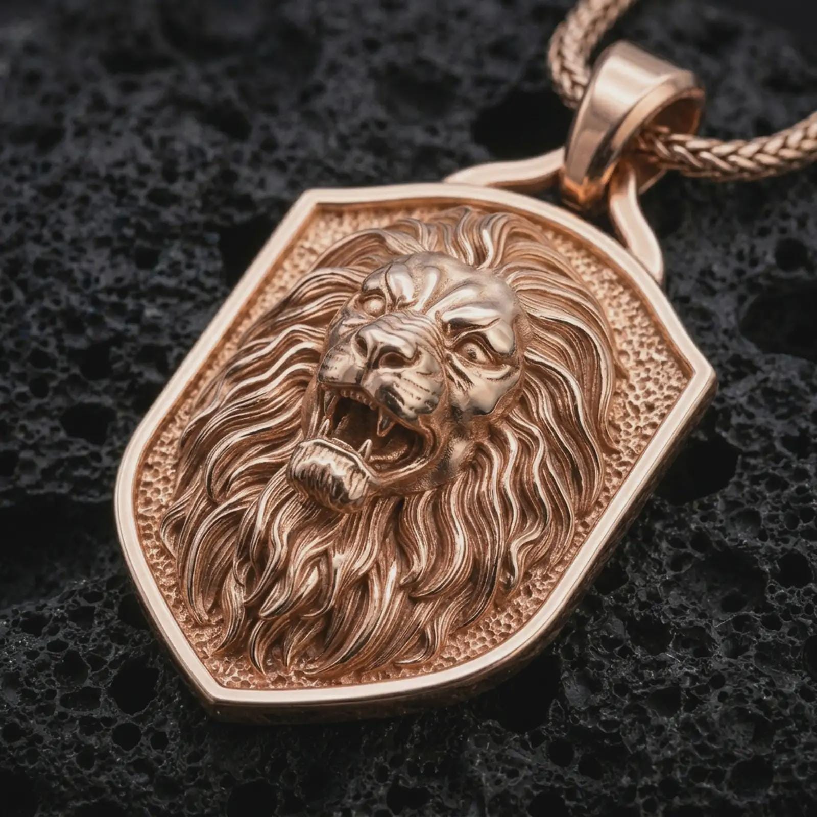 Rose gold plated roaring lion shield pendant necklace on dark volcanic rock, photographed in a detailed premium studio macro view.