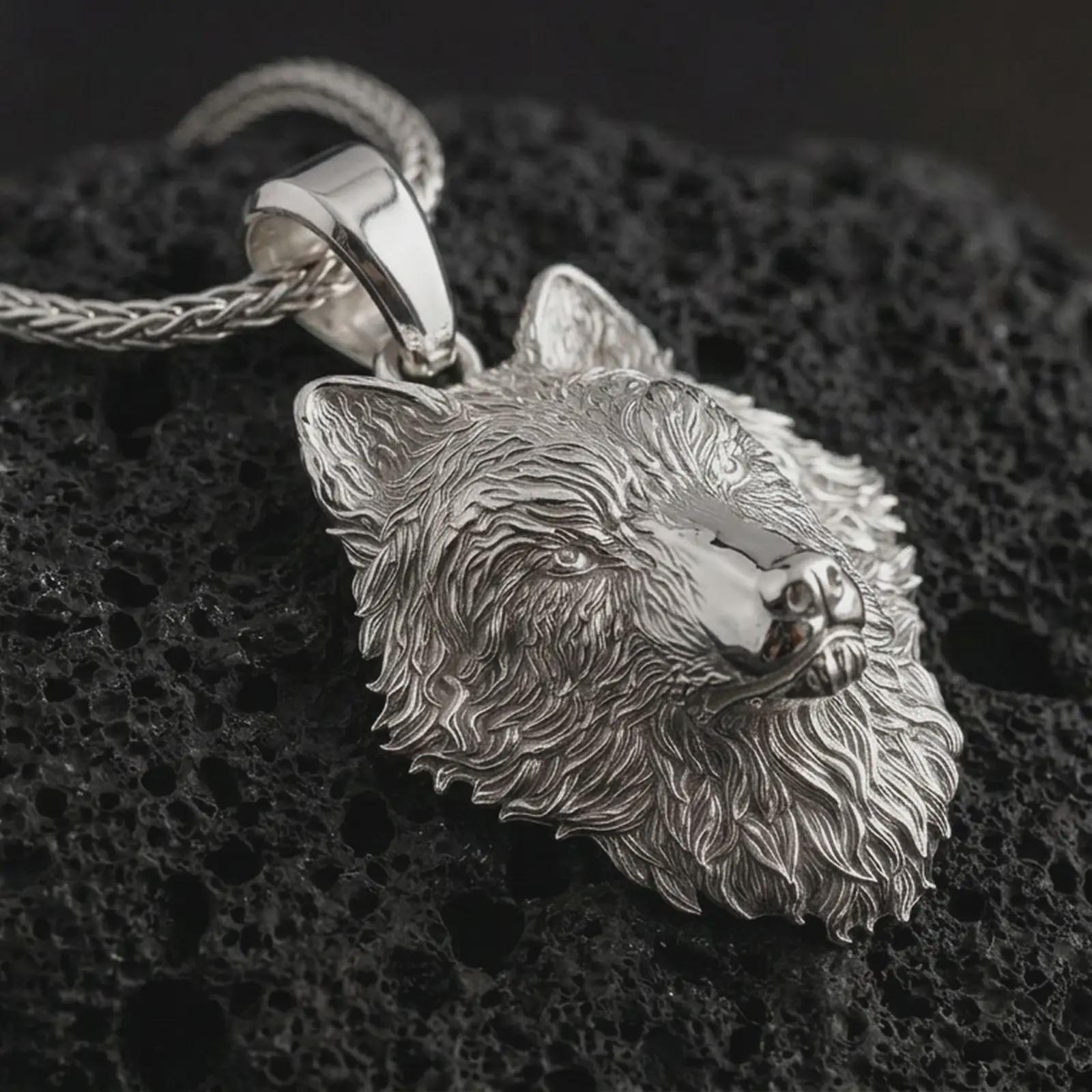 Polished silver wolf head pendant necklace displayed on black volcanic rock, shown in a refined macro product shot with detailed fur texture, alert ears, and intense predatory gaze.