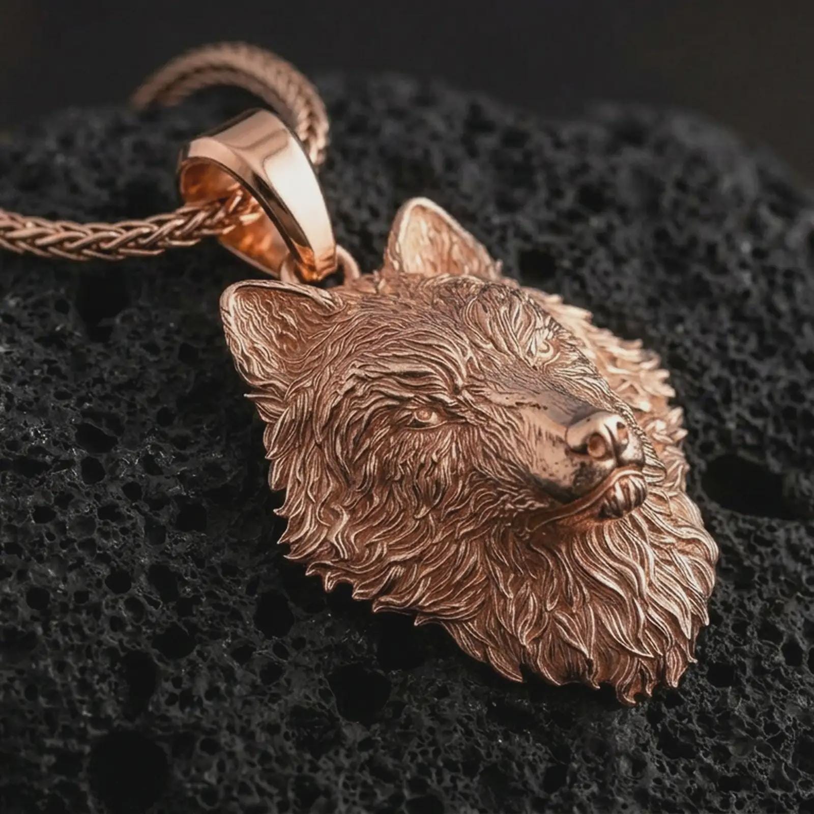 Rose gold plated wolf head pendant necklace on dark volcanic rock, photographed in a detailed premium studio macro view.