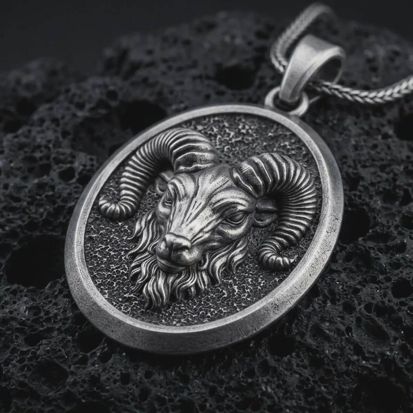 Sterling silver ram head pendant necklace with an oxidized finish resting on textured volcanic rock, captured in a close-up premium studio composition.