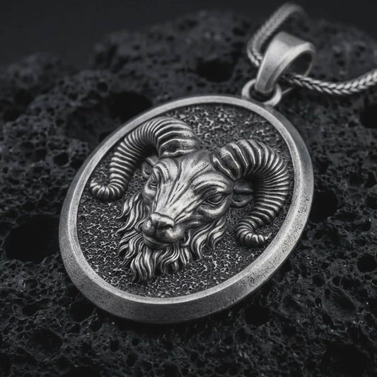 Sterling silver ram head pendant necklace with an oxidized finish resting on textured volcanic rock, captured in a close-up premium studio composition.