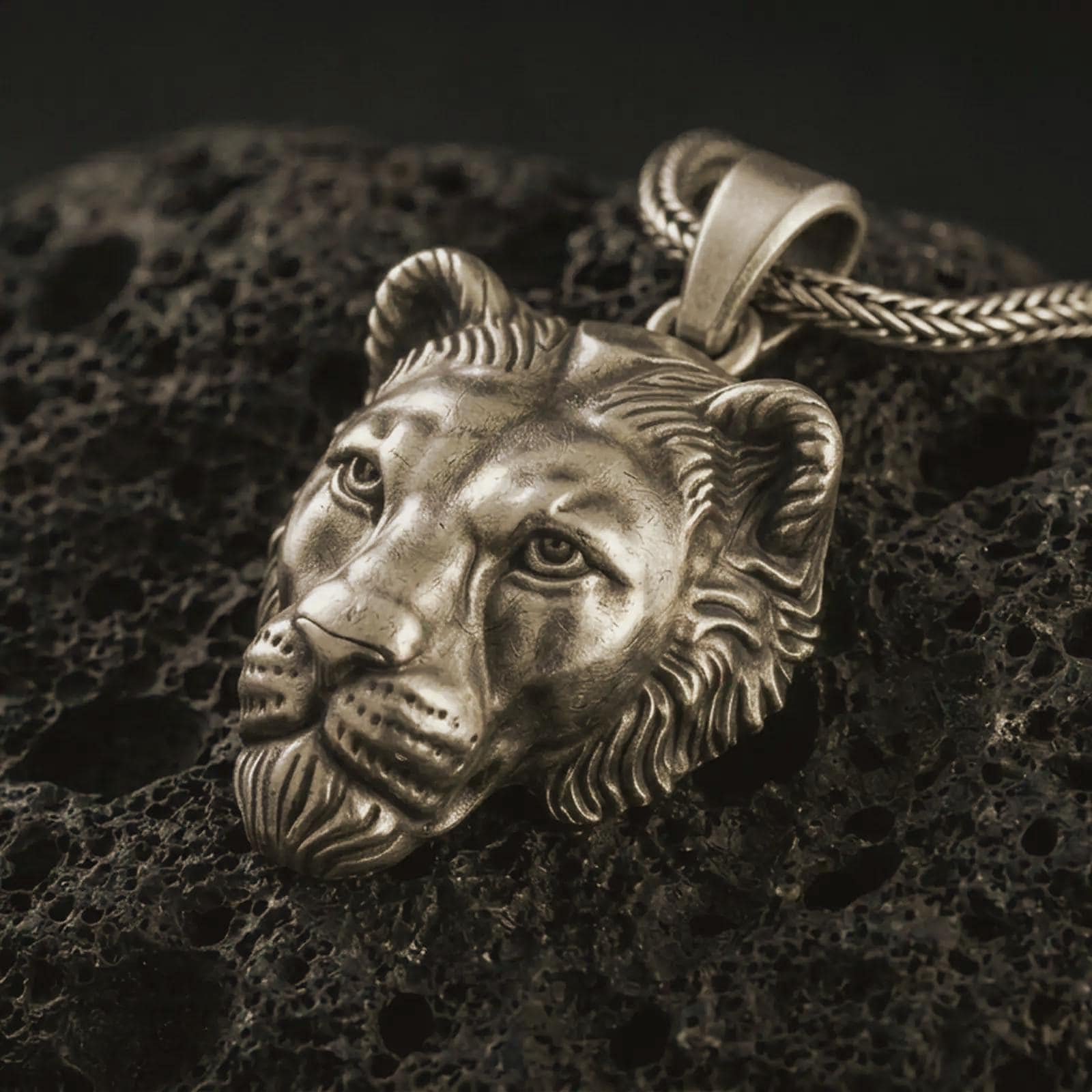 Bronze 3D lioness pendant necklace with an oxidized finish resting on textured volcanic rock, captured in a close-up premium studio composition.