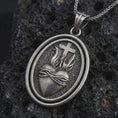 Load image into Gallery viewer, Oxidized Sacred Heart pendant necklace on textured volcanic rock, close-up studio shot highlighting the flaming heart, crown of thorns, cross, and antique silver contrast.
