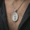 Load image into Gallery viewer, Polished silver Our Lady of Guadalupe spinner pendant necklace worn on the chest, masculine lifestyle shot highlighting the Virgin Mary relief, crescent moon, and bright silver finish.
