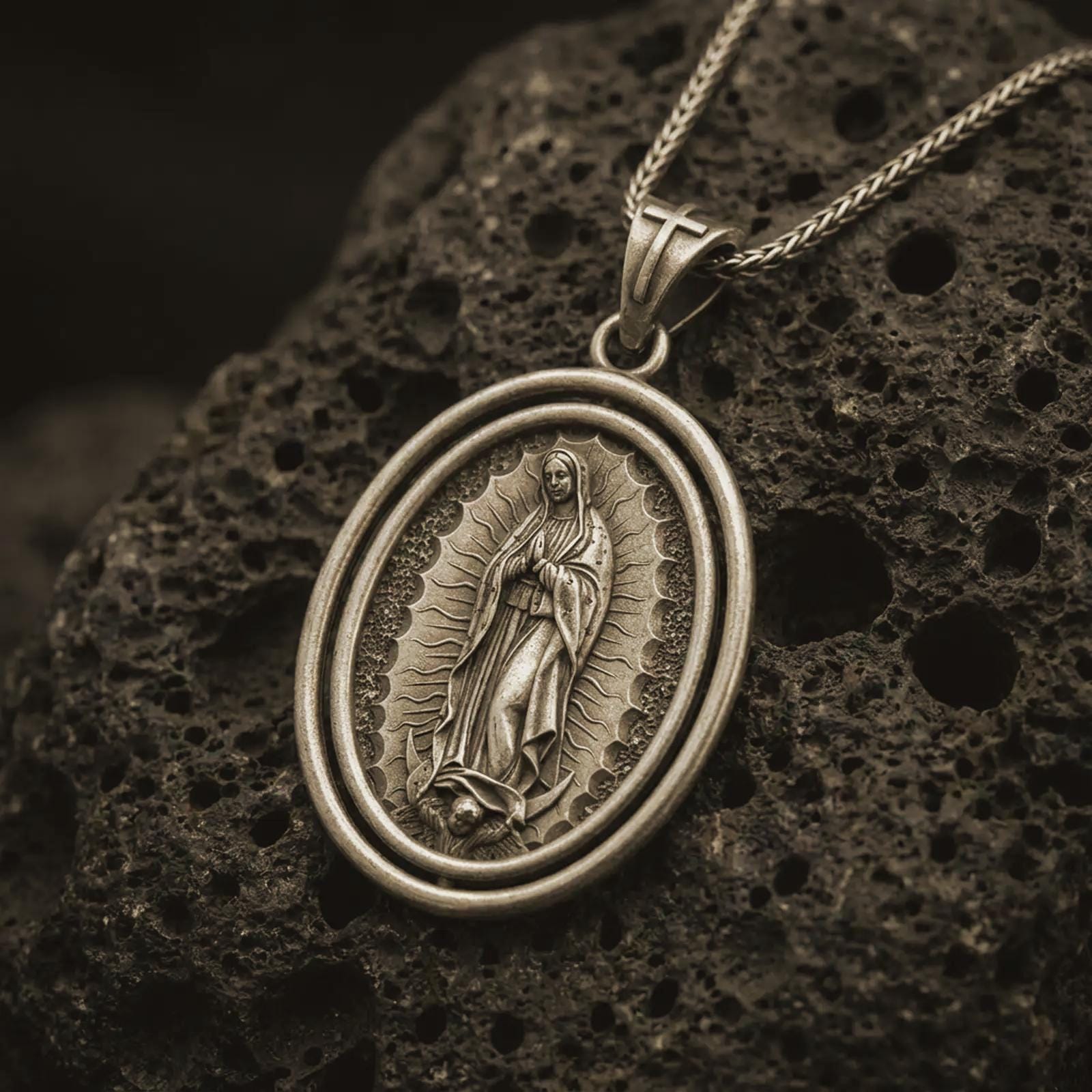 Bronze Our Lady of Guadalupe spinner pendant necklace on textured volcanic rock, close-up studio shot highlighting the Virgin Mary relief, radiant halo, crescent moon, and antique silver contrast.