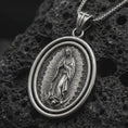 Load image into Gallery viewer, Oxidized Our Lady of Guadalupe spinner pendant necklace on textured volcanic rock, close-up studio shot highlighting the Virgin Mary relief, radiant halo, crescent moon, and antique silver contrast.

