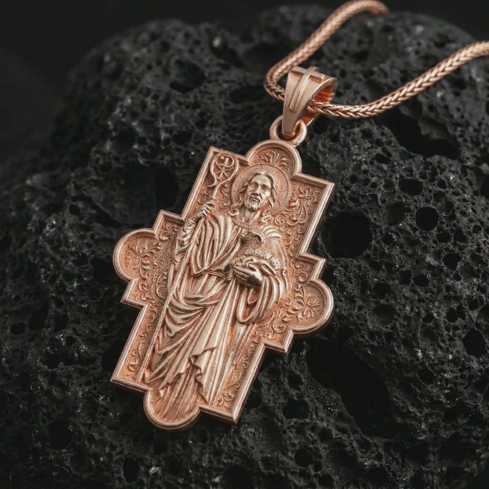 Rose gold plated Good Shepherd cross pendant necklace on textured volcanic rock, detailed macro product shot with soft warm reflections and sacred shepherd symbolism.