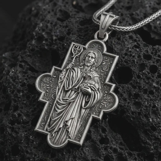 Oxidized Good Shepherd cross pendant necklace on textured volcanic rock, close-up studio shot highlighting the Jesus relief, lamb, shepherd staff, ornate cross frame, and antique silver contrast.