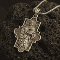Load image into Gallery viewer, Bronze Good Shepherd cross pendant necklace on textured volcanic rock, close-up studio shot highlighting the Jesus relief, lamb, shepherd staff, ornate cross frame, and antique silver contrast.
