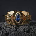 Load image into Gallery viewer, A sterling silver ring with a gold plated finish and marquise blue stone displayed on textured volcanic rock in a premium macro shot.
