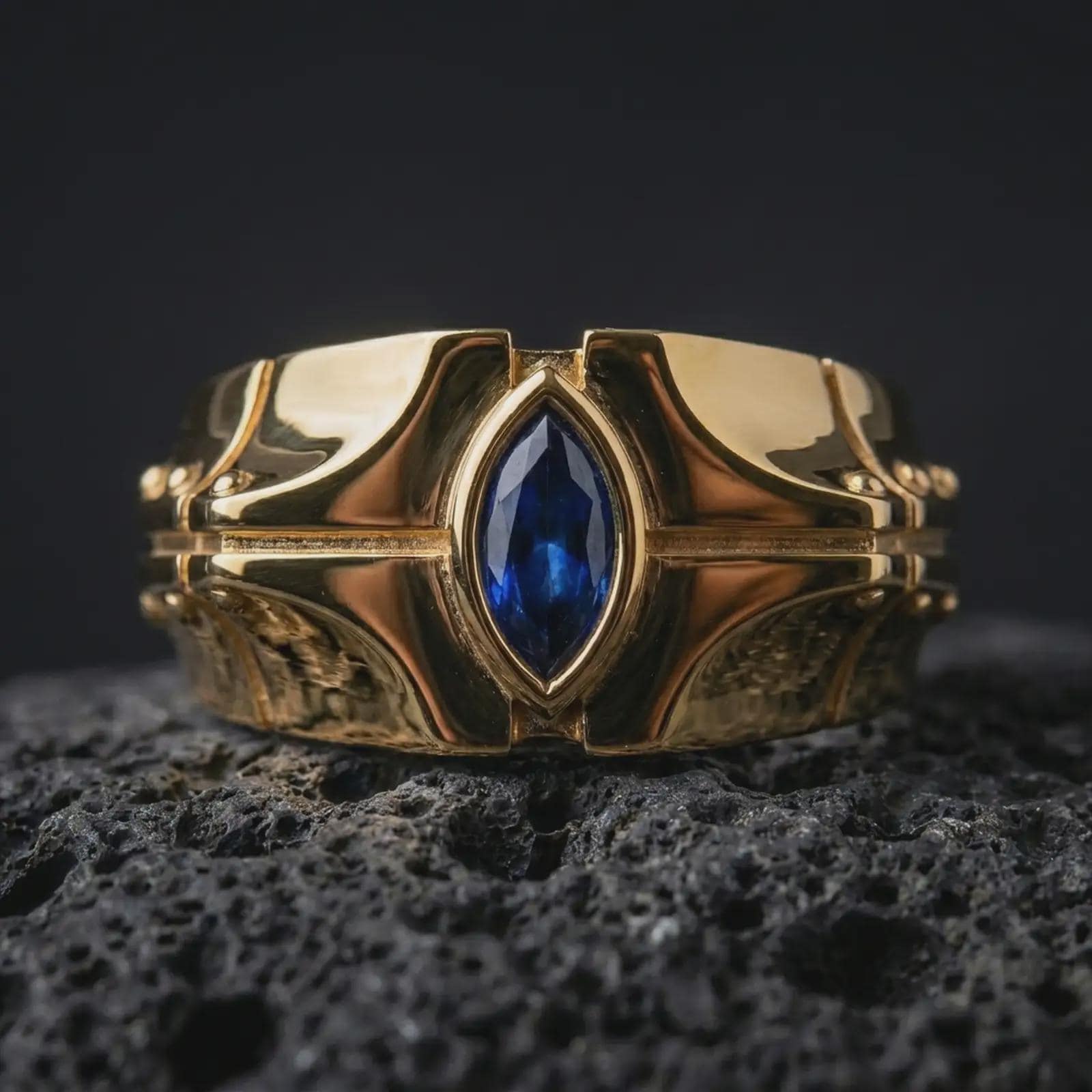 A sterling silver ring with a gold plated finish and marquise blue stone displayed on textured volcanic rock in a premium macro shot.