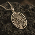 Load image into Gallery viewer, Bronze Saint Christopher spinning pendant necklace on textured volcanic rock, close-up studio shot highlighting the saint carrying child Jesus, staff detail, rotating frame, and antique silver contrast.

