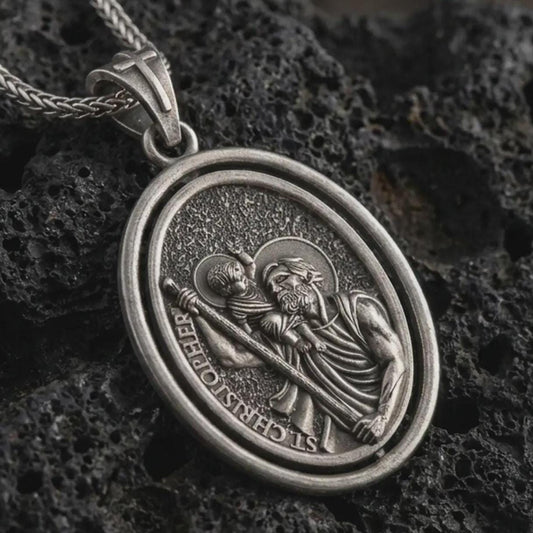 Oxidized Saint Christopher spinning pendant necklace on textured volcanic rock, close-up studio shot highlighting the saint carrying child Jesus, staff detail, rotating frame, and antique silver contrast.
