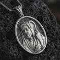 Load image into Gallery viewer, Oxidized Jesus Christ Good Shepherd pendant necklace on textured volcanic rock, close-up studio shot highlighting the shepherd portrait, hooded robe, staff detail, and antique silver contrast.
