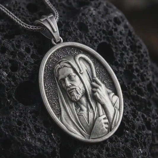 Oxidized Jesus Christ Good Shepherd pendant necklace on textured volcanic rock, close-up studio shot highlighting the shepherd portrait, hooded robe, staff detail, and antique silver contrast.