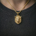 Load image into Gallery viewer, Gold plated bull head shield pendant necklace worn on the neck, captured on a human model in a premium dark-toned lifestyle frame.

