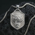 Load image into Gallery viewer, Polished silver roaring lion shield pendant necklace displayed on black volcanic rock, shown in a refined macro product shot with fierce open jaws, fang detail, and sculpted shield frame.
