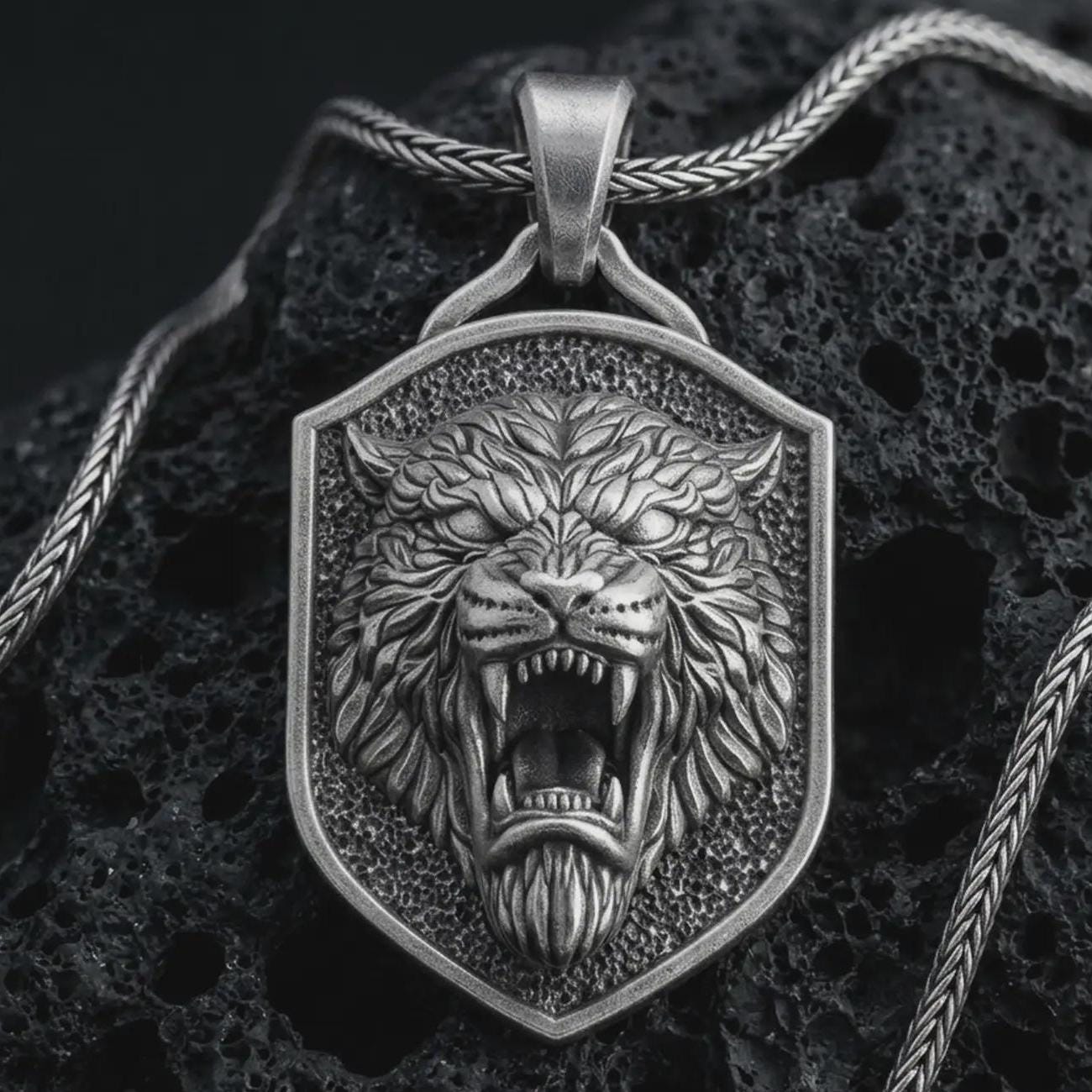 Sterling silver roaring lion shield pendant necklace with an oxidized finish resting on textured volcanic rock, captured in a close-up premium studio composition.