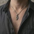 Load image into Gallery viewer, Oxidized Pegasus wing horse pendant necklace worn on the neck, styled in a dark lifestyle portrait with an open shirt and graceful fantasy-inspired presentation.
