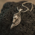 Load image into Gallery viewer, Bronze Pegasus wing horse pendant necklace with an oxidized finish resting on textured volcanic rock, captured in a close-up premium studio composition.
