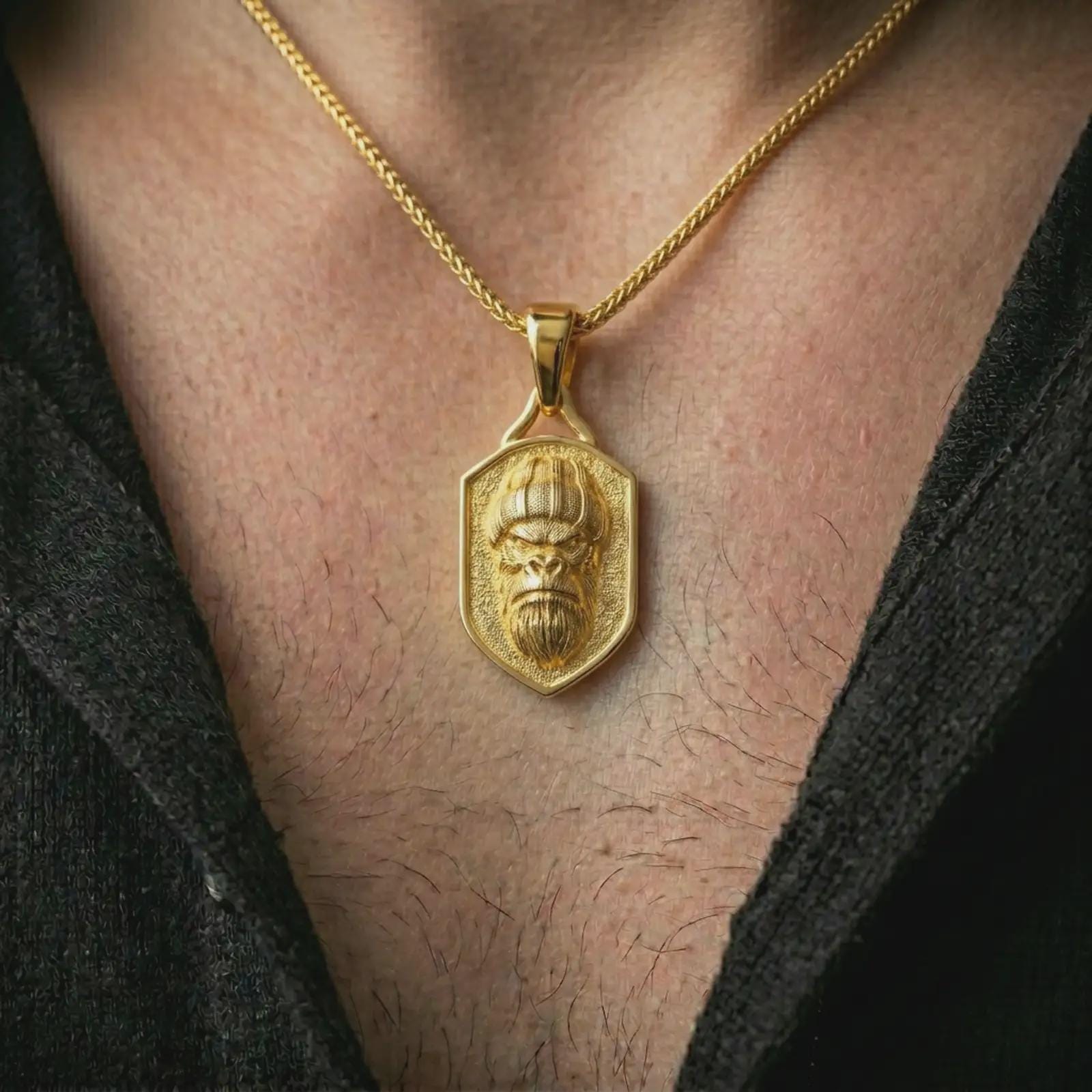 Gold plated gorilla shield pendant necklace worn on the neck, captured on a human model in a premium dark-toned lifestyle frame.