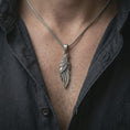 Load image into Gallery viewer, Oxidized raven pendant necklace worn on the neck, styled in a dark lifestyle portrait with an open shirt and bold Viking-inspired presentation.
