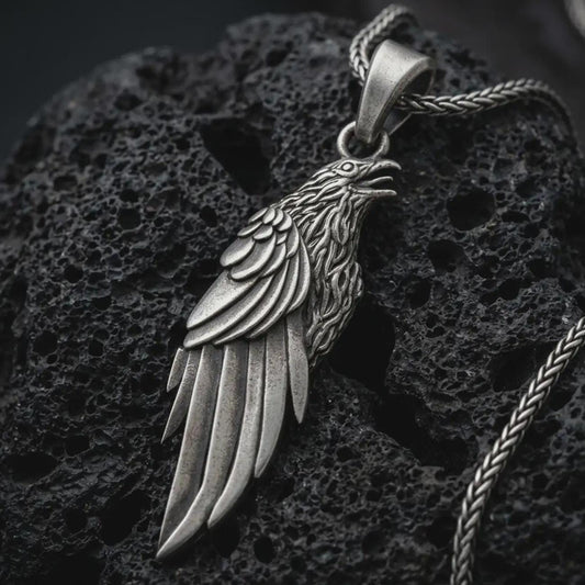 Sterling silver raven pendant necklace with an oxidized finish resting on textured volcanic rock, captured in a close-up premium studio composition.