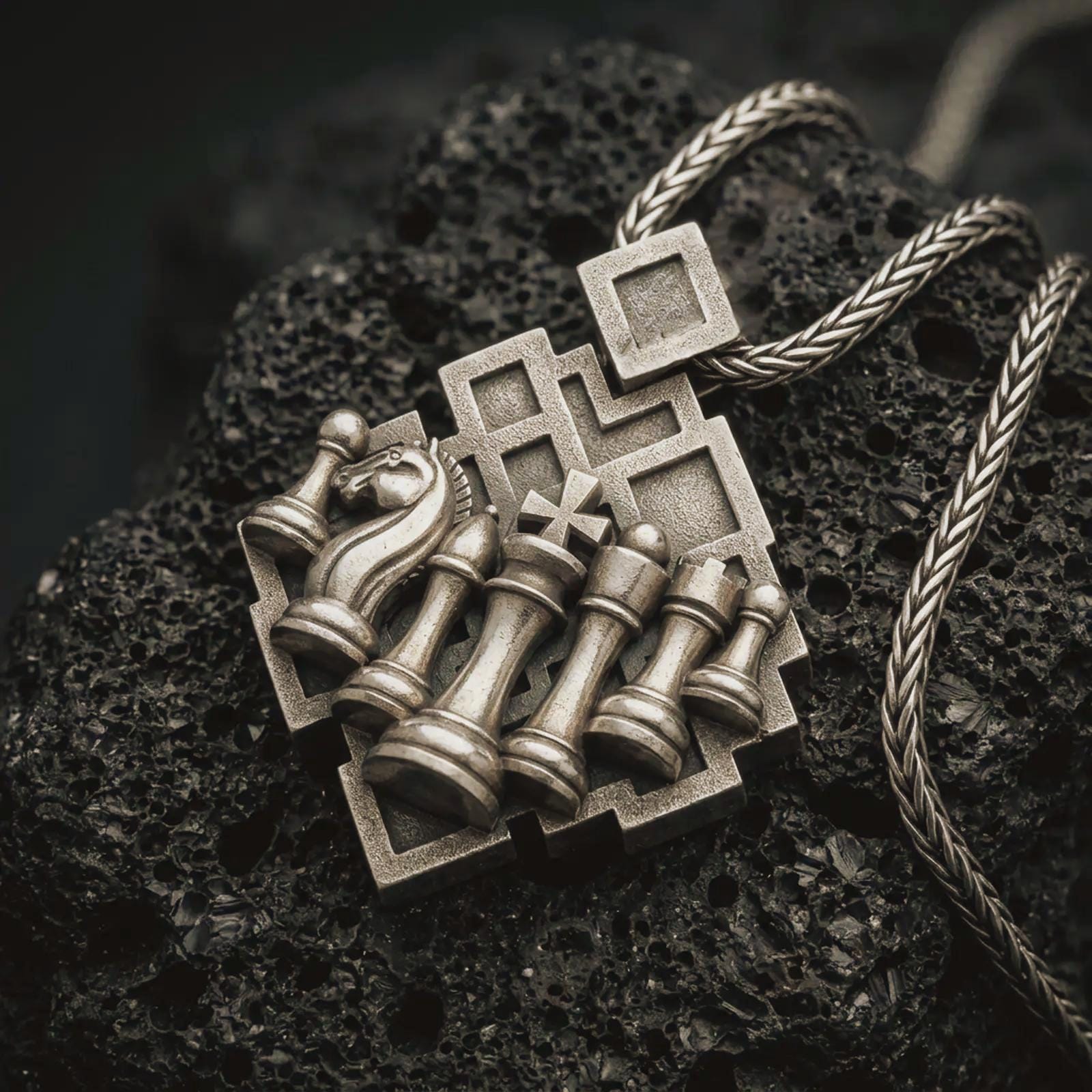 Bronze chessboard pendant necklace with an oxidized finish resting on textured volcanic rock, captured in a close-up premium studio composition.