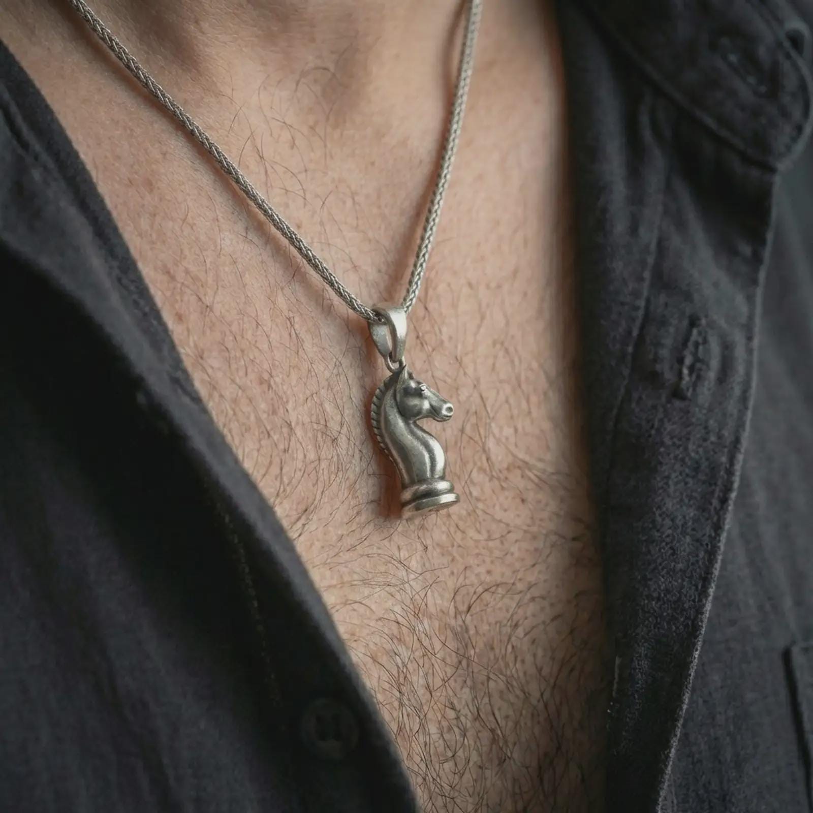 Oxidized knight chess piece pendant necklace worn on the neck, styled in a dark lifestyle portrait with an open shirt and bold intellectual presentation.