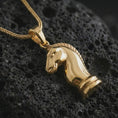 Load image into Gallery viewer, Gold plated knight chess piece pendant necklace presented on porous volcanic rock, highlighting the strategic chess motif in a luxurious close-up jewelry image.
