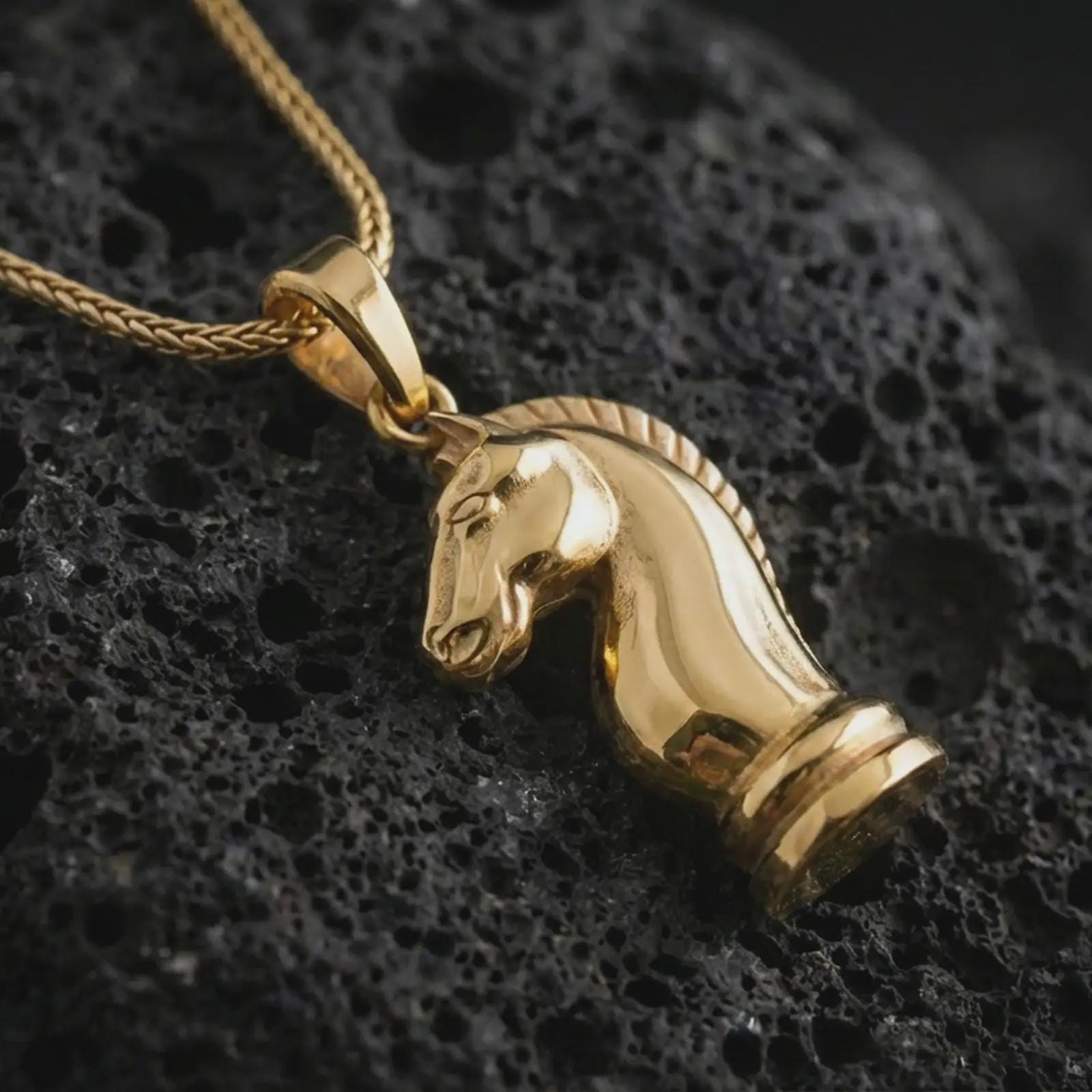 Gold plated knight chess piece pendant necklace presented on porous volcanic rock, highlighting the strategic chess motif in a luxurious close-up jewelry image.