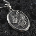 Load image into Gallery viewer, Sterling silver wolf medallion pendant necklace with an oxidized finish resting on textured volcanic rock, captured in a close-up premium studio composition.
