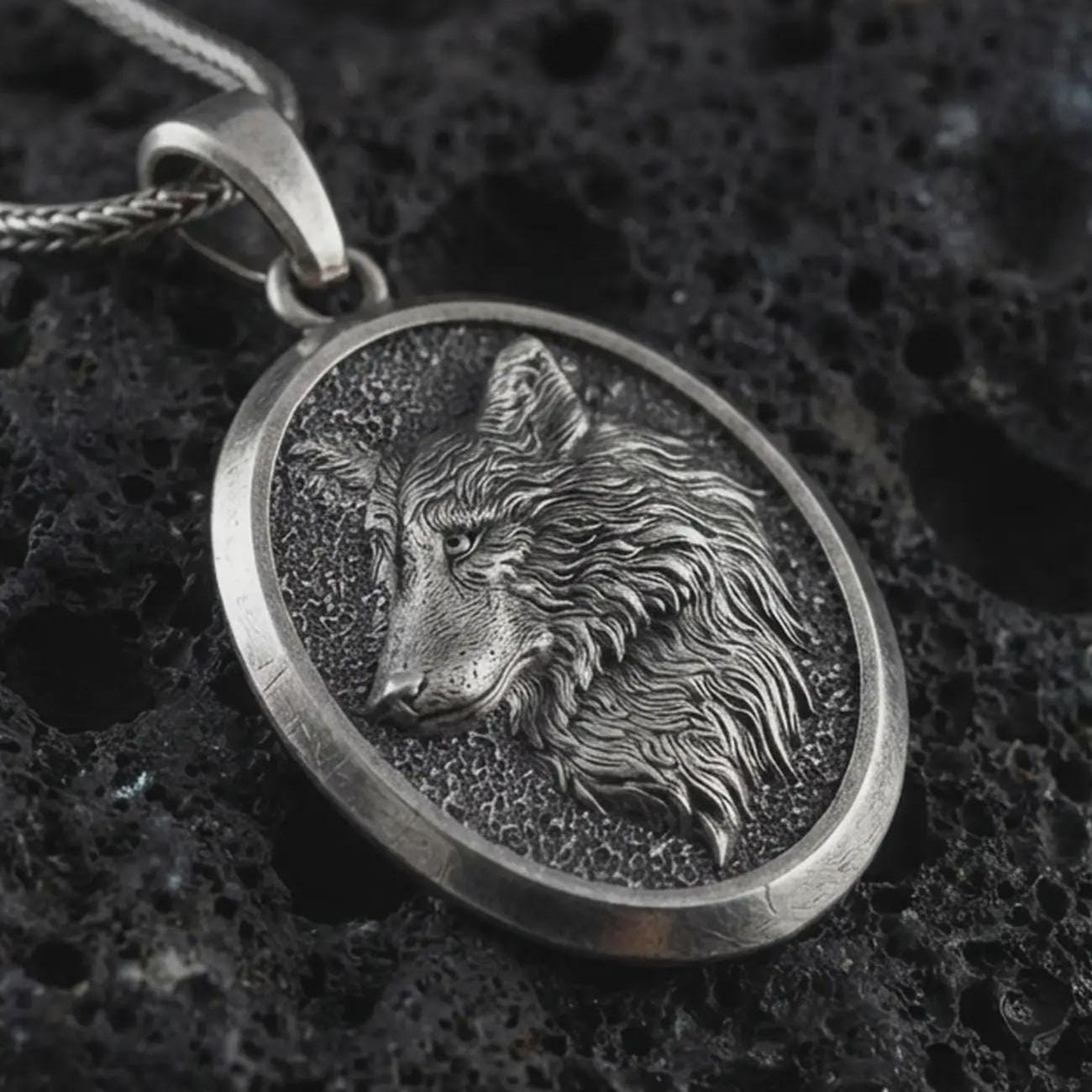 Sterling silver wolf medallion pendant necklace with an oxidized finish resting on textured volcanic rock, captured in a close-up premium studio composition.