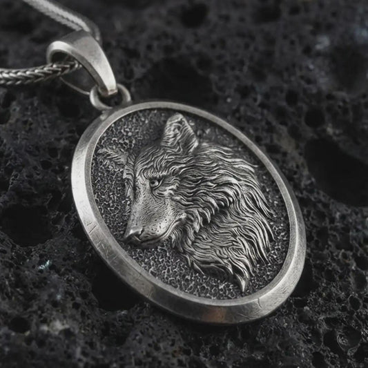 Sterling silver wolf medallion pendant necklace with an oxidized finish resting on textured volcanic rock, captured in a close-up premium studio composition.