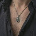 Load image into Gallery viewer, Oxidized lion shield pendant necklace worn on the neck, styled in a dark lifestyle portrait with an open shirt and bold noble presentation.

