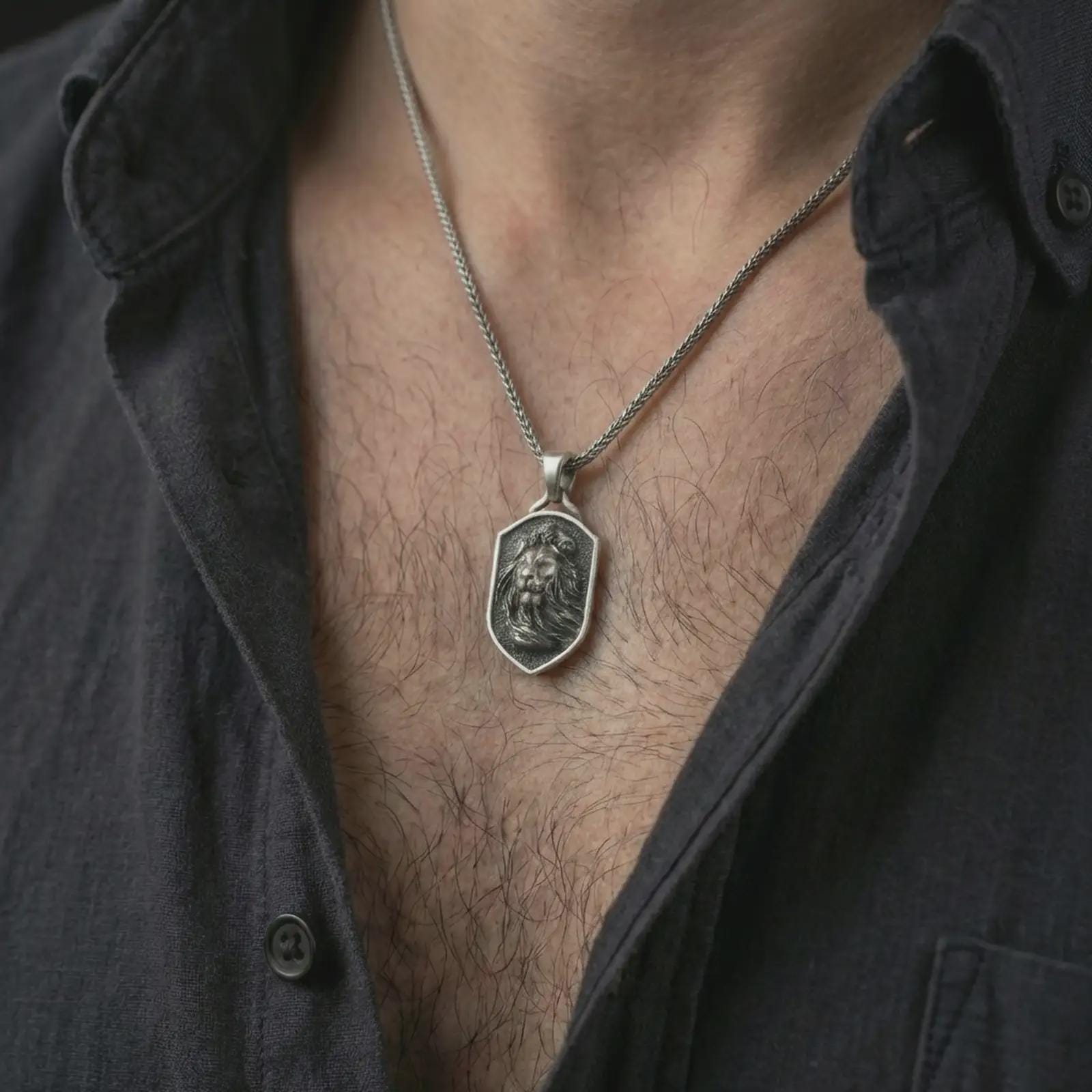 Oxidized lion shield pendant necklace worn on the neck, styled in a dark lifestyle portrait with an open shirt and bold noble presentation.