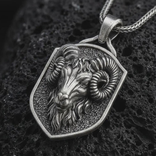 Sterling silver ram head shield pendant necklace with an oxidized finish resting on textured volcanic rock, captured in a close-up premium studio composition.