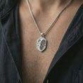 Load image into Gallery viewer, Ram head shield pendant necklace in polished silver worn on the neck, presented in a clean close-up model image with a strong masculine and zodiac-focused look.

