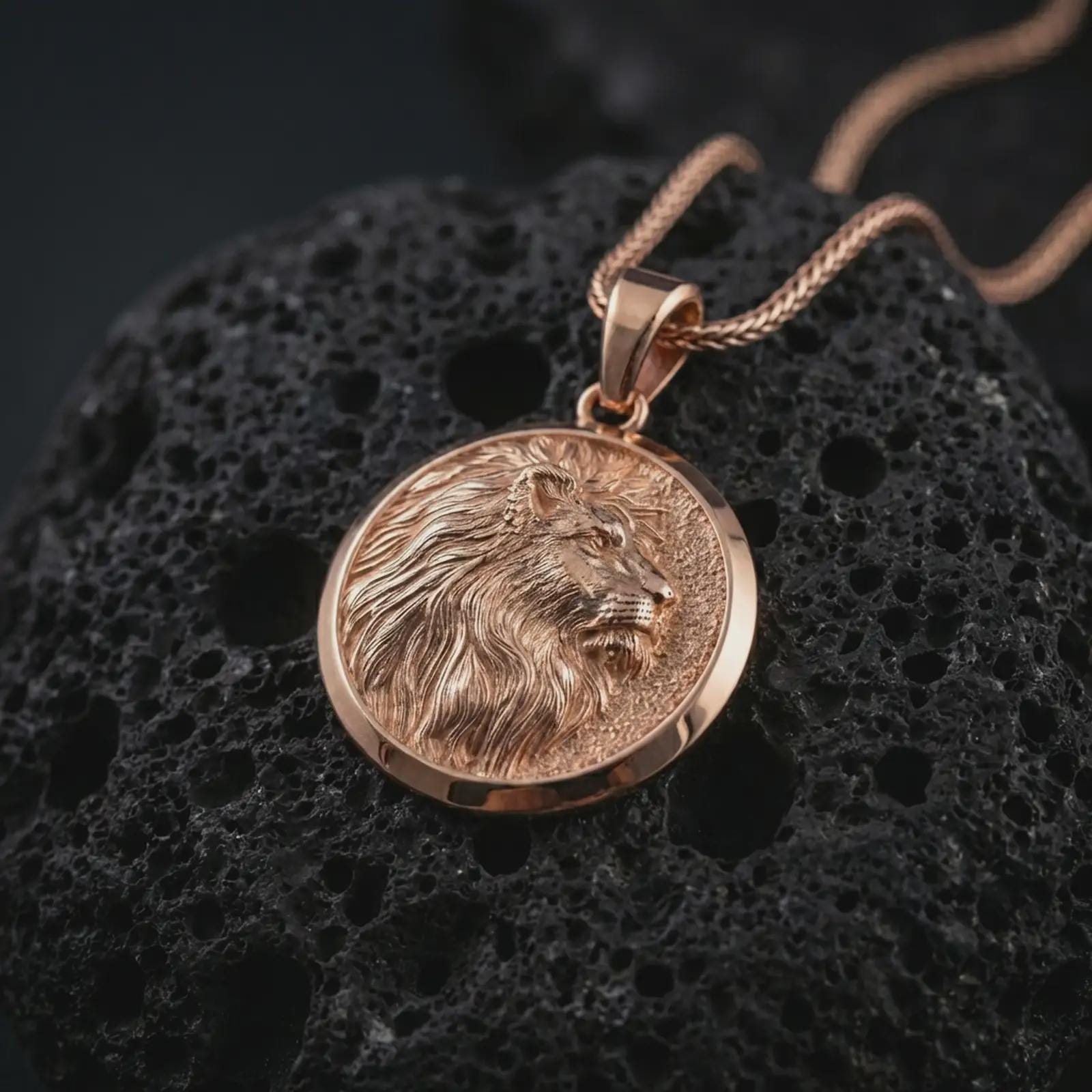 Rose gold plated lion medallion pendant necklace on dark volcanic rock, shown in a premium macro studio view with a bold round medallion silhouette and majestic lion profile.