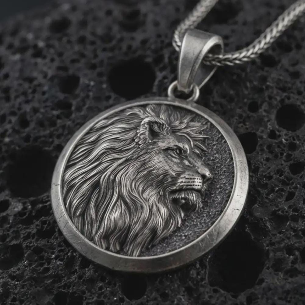 Sterling silver lion medallion pendant necklace with an oxidized finish resting on textured volcanic rock, captured in a close-up premium studio composition.