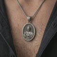 Load image into Gallery viewer, Oxidized Saint Francis pendant necklace worn on the chest, close-up lifestyle jewelry photo showing the Catholic medallion on a spiga chain with dark clothing.
