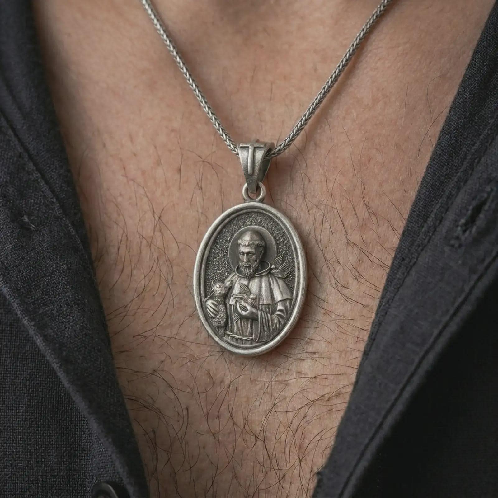 Oxidized Saint Francis pendant necklace worn on the chest, close-up lifestyle jewelry photo showing the Catholic medallion on a spiga chain with dark clothing.