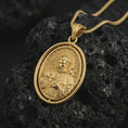 Load image into Gallery viewer, Gold plated Saint Francis pendant necklace on textured volcanic rock, premium close-up studio composition emphasizing the saint figure, lamb, birds, and nature symbolism.
