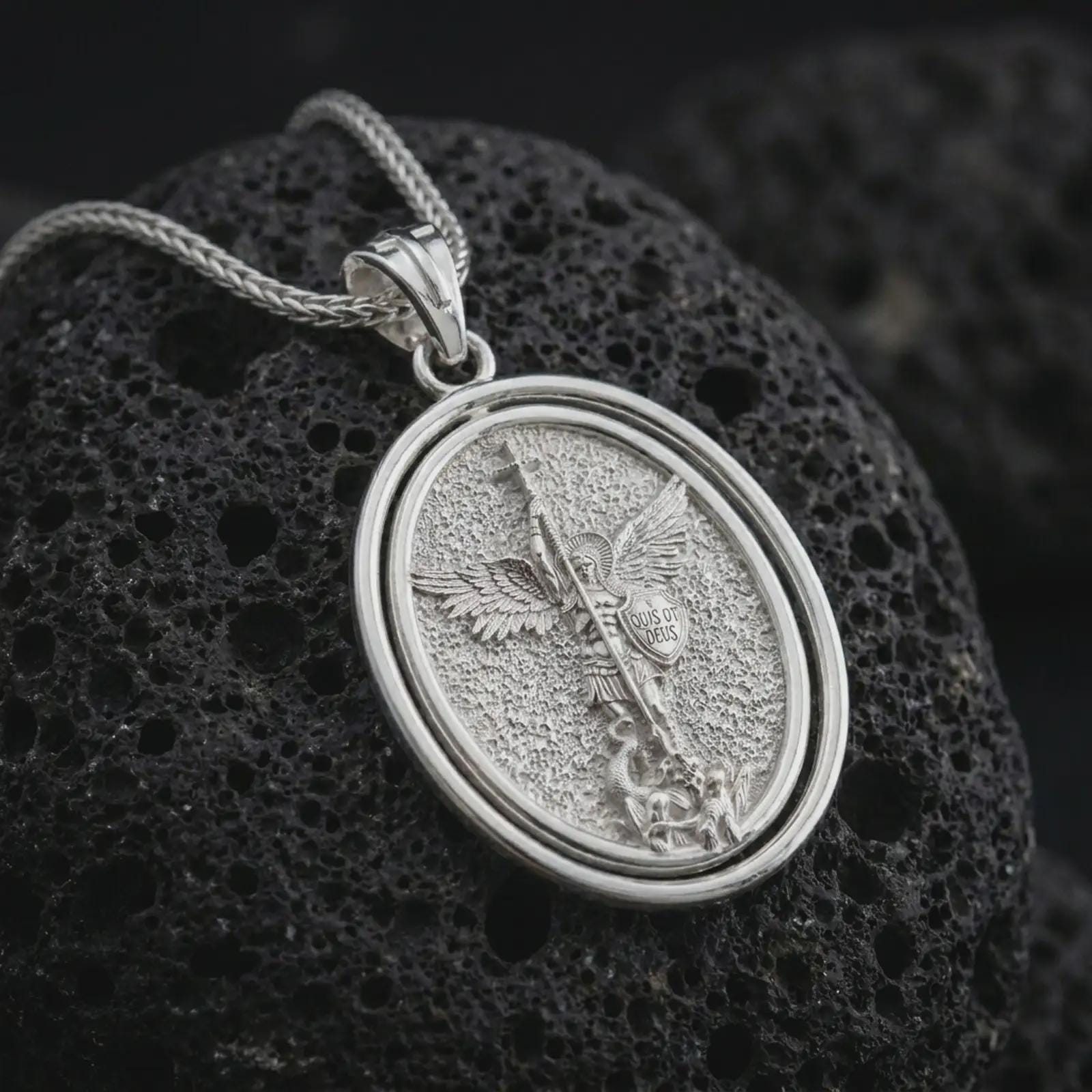 Polished silver Saint Michael spinning pendant necklace on textured volcanic rock, centered macro jewelry photo with detailed archangel relief and bright silver highlights.