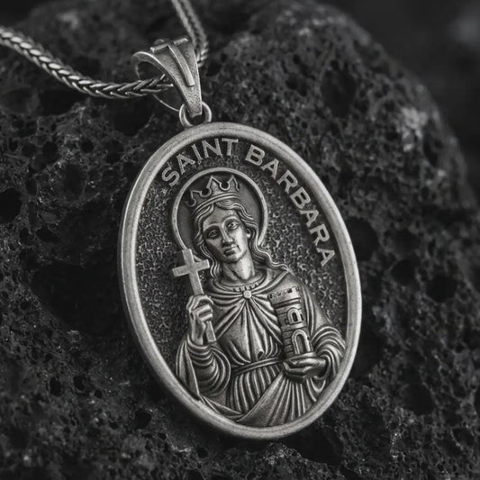 Oxidized Saint Barbara pendant necklace on textured volcanic rock, close-up studio shot highlighting the crowned saint relief, cross, tower detail, and antique silver contrast.