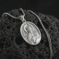 Load image into Gallery viewer, Polished silver Saint James the Apostle pendant necklace on textured volcanic rock, centered macro jewelry photo with detailed religious medal engraving and bright silver highlights.
