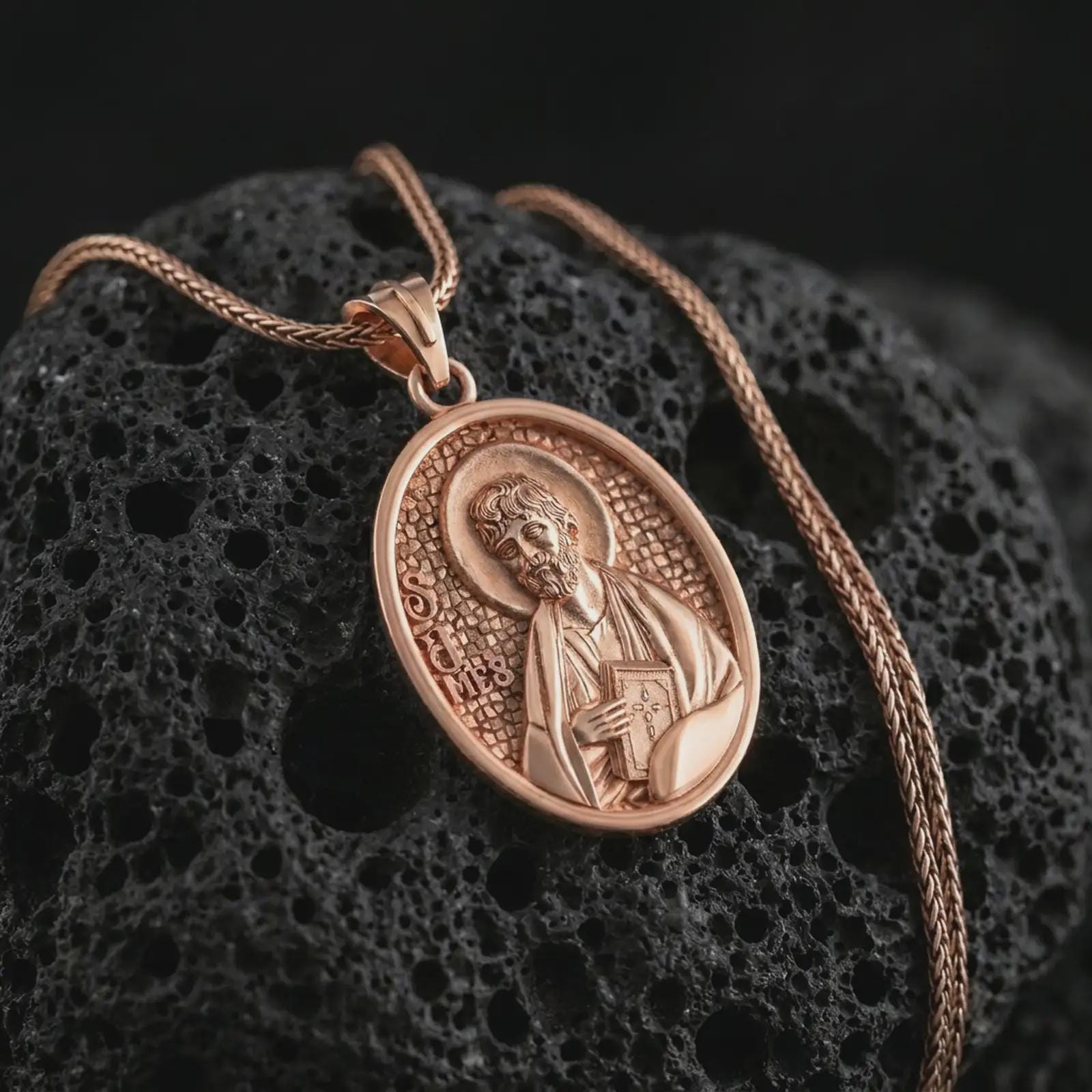 Rose gold plated Saint James the Apostle pendant necklace on textured volcanic rock, detailed macro product shot with soft warm reflections and devotional Saint James design.