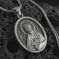 Load image into Gallery viewer, Oxidized Saint James the Apostle pendant necklace on textured volcanic rock, close-up studio shot highlighting the apostle relief, halo, book detail, and antique silver contrast.
