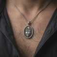 Load image into Gallery viewer, Oxidized Sacred Heart pendant necklace worn on the chest, close-up lifestyle jewelry photo showing the Catholic heart medallion on a spiga chain with dark clothing.
